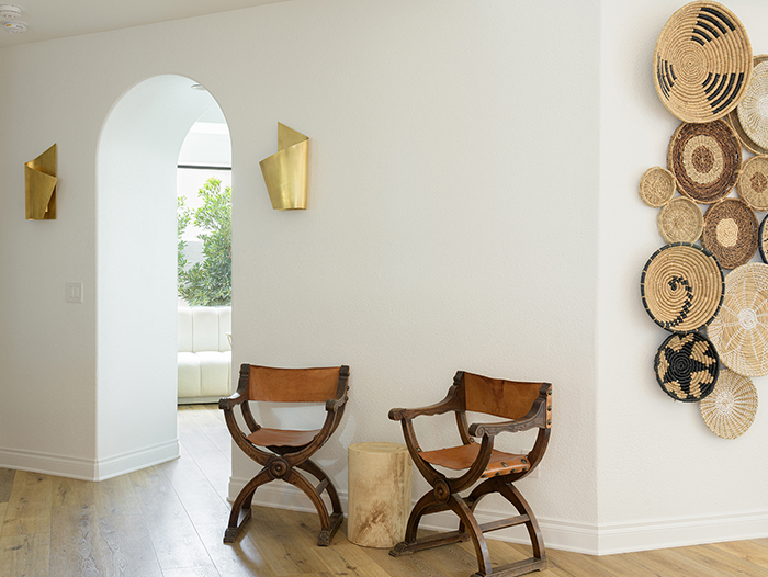 Curved wood-and-leather chairs against white wall. Collection of woven baskets form artwork on the wall around the corner.